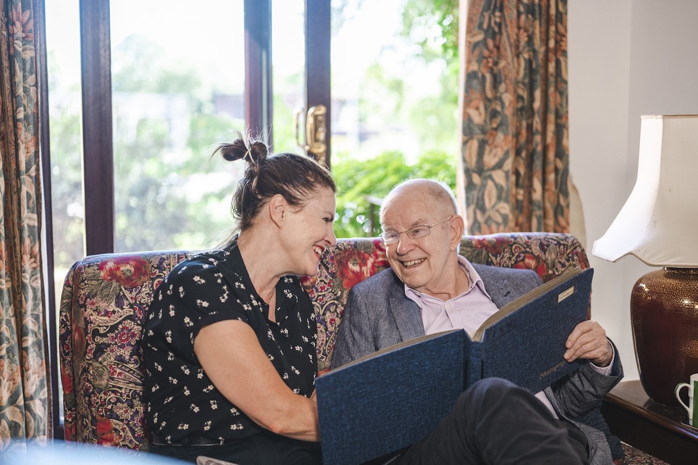 An Overcome caregiver sharing a warm moment with a client over a photo album at home
